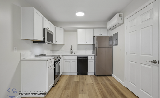 A kitchen with white cabinets and appliances, a wooden floor, and a door on the right.